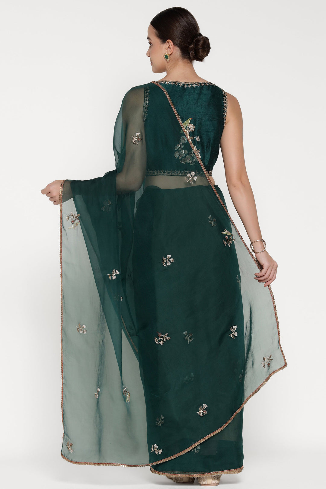 Woman wearing a dark green saree with floral patterns on a white background