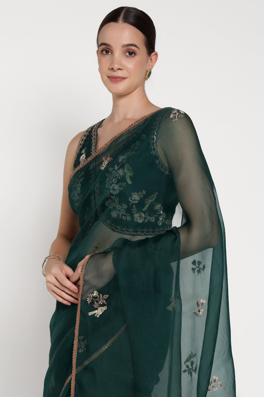 Woman wearing a dark green saree with floral embroidery on a white background