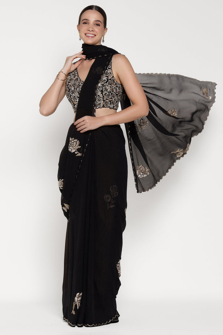 Woman wearing a black saree with gold embroidery on a white background