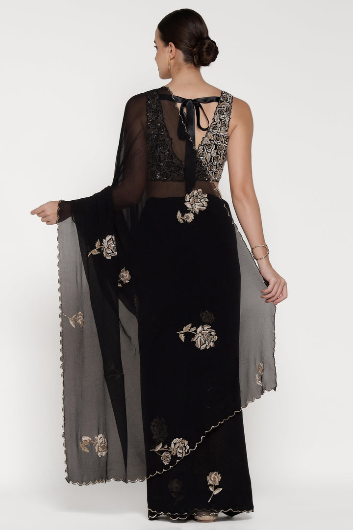 Woman wearing a black saree with floral embroidery on a white background