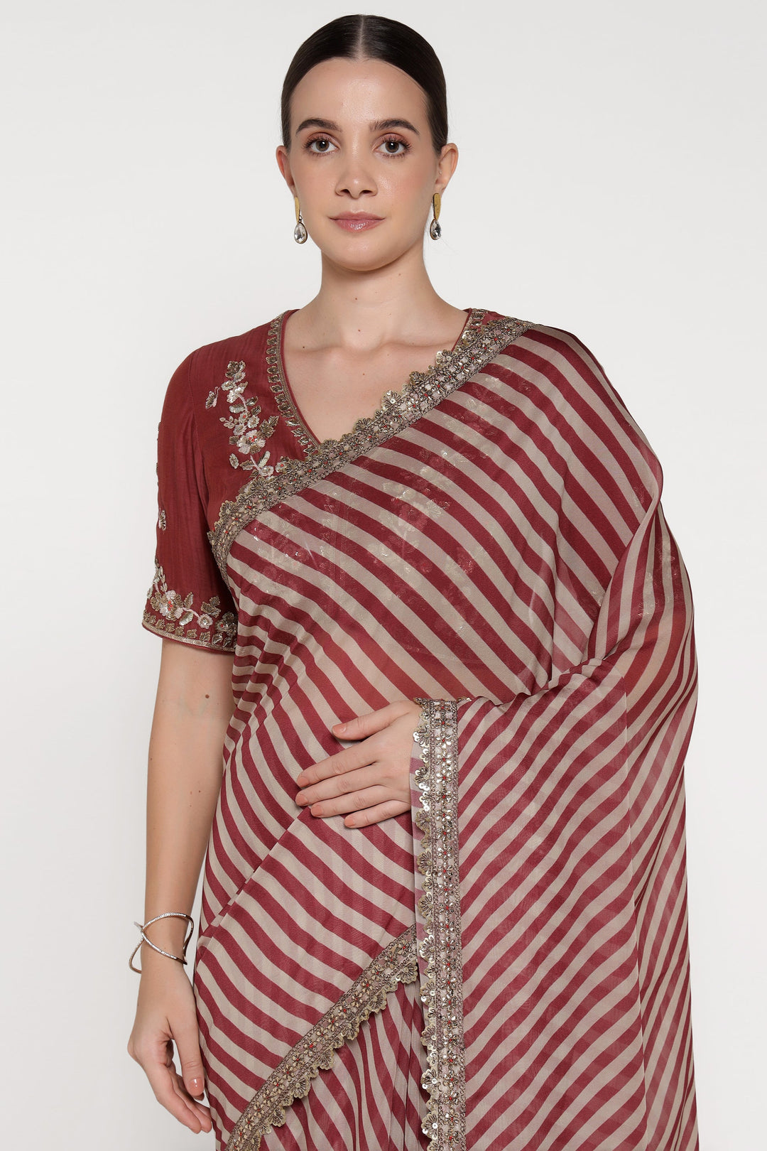 Woman wearing a maroon and white striped saree with intricate border on a plain background