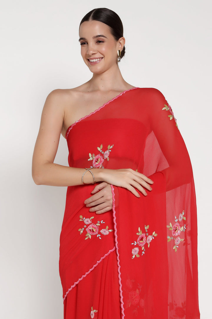 Woman wearing a red saree with floral embroidery on a white background