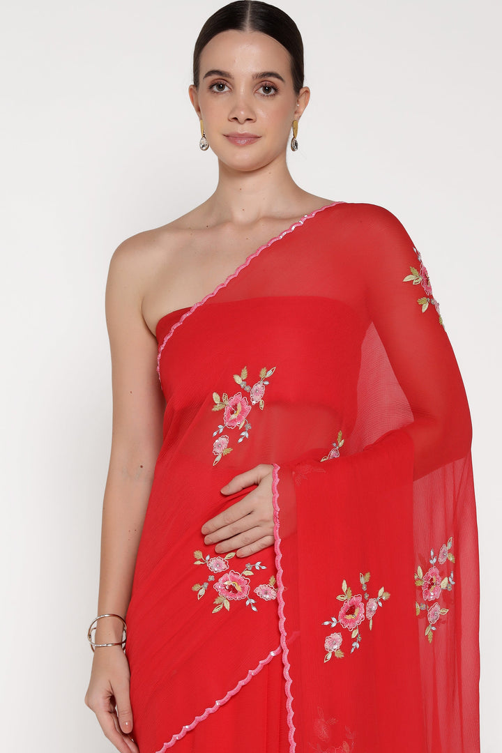 Woman wearing a red saree with floral embroidery on a white background