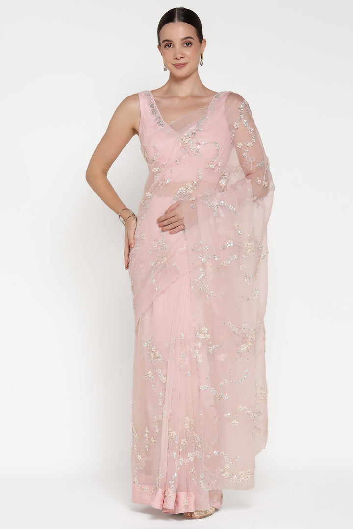 Woman wearing a light pink saree with floral patterns on a white background