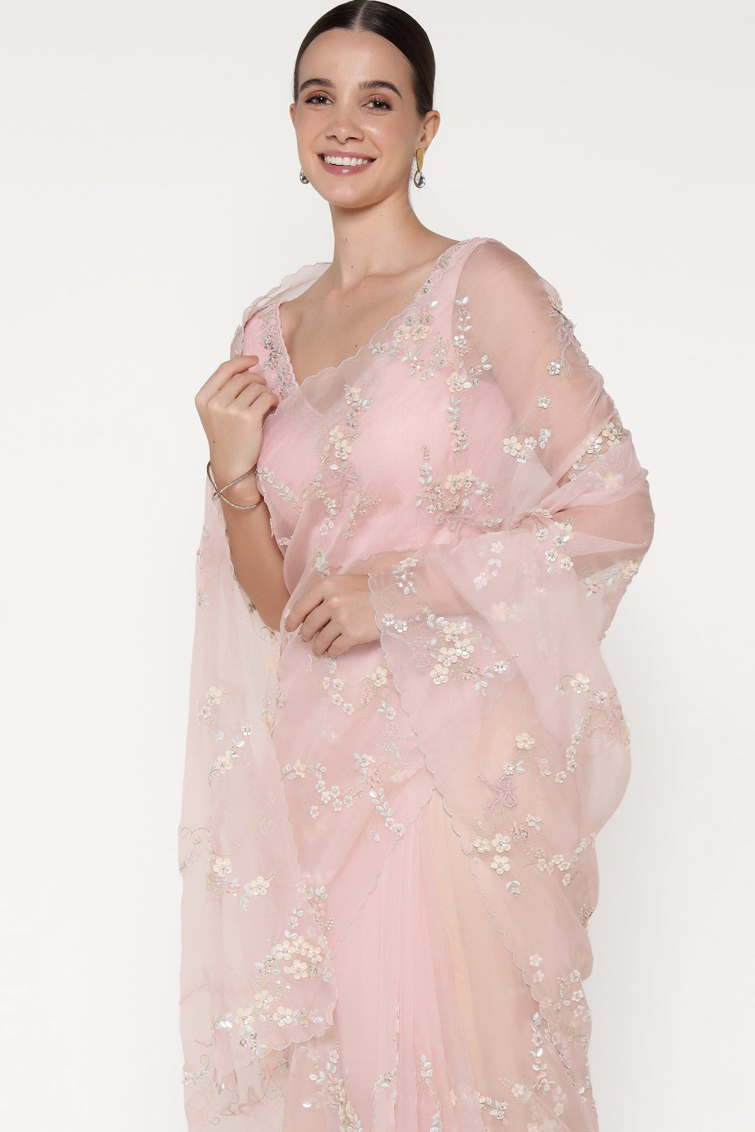 Woman wearing a light pink saree with floral patterns on a white background