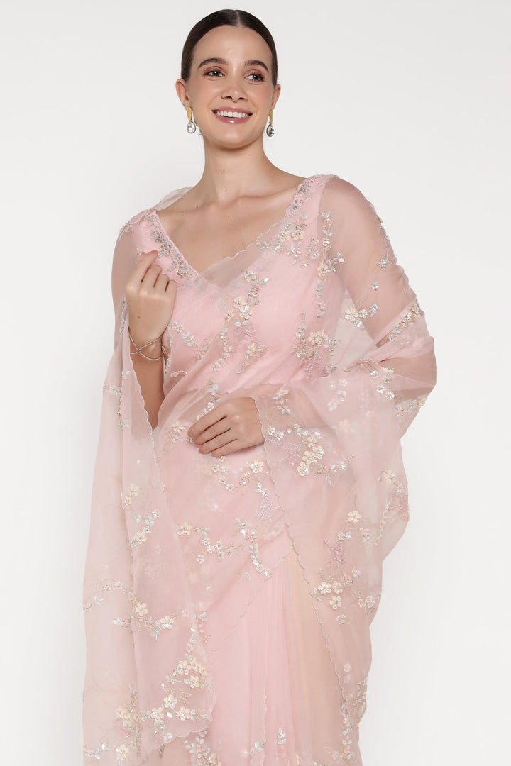 Woman wearing a light pink saree with floral patterns on a white background