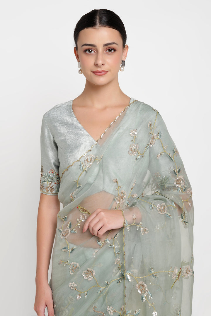 Woman wearing a light green saree with floral embroidery on a white background