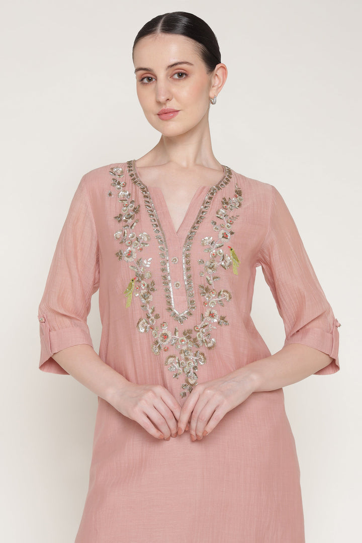 Woman wearing a pink embroidered dress against a white background