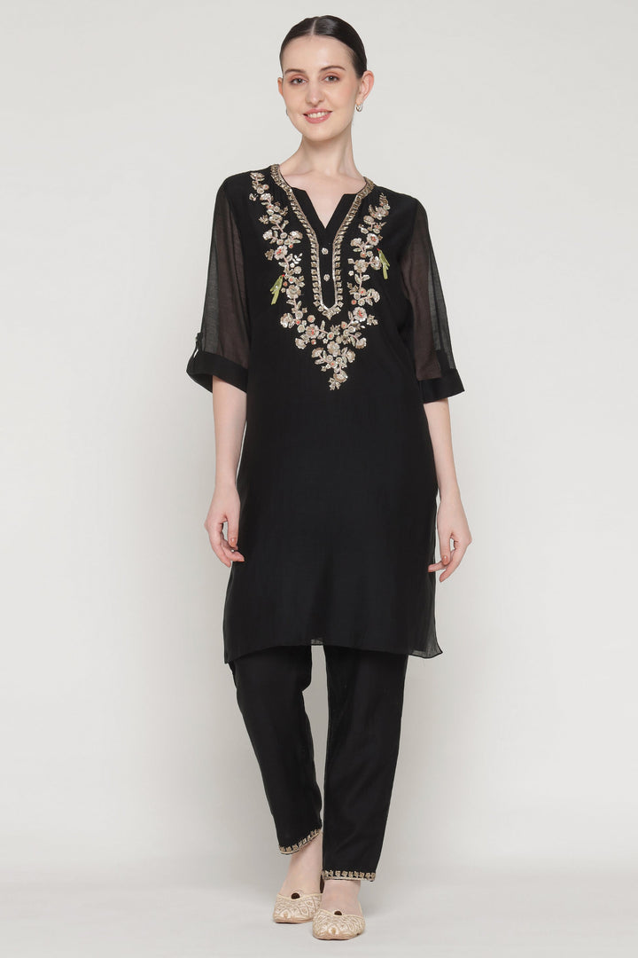 Woman wearing a black outfit with gold embroidery on a white background