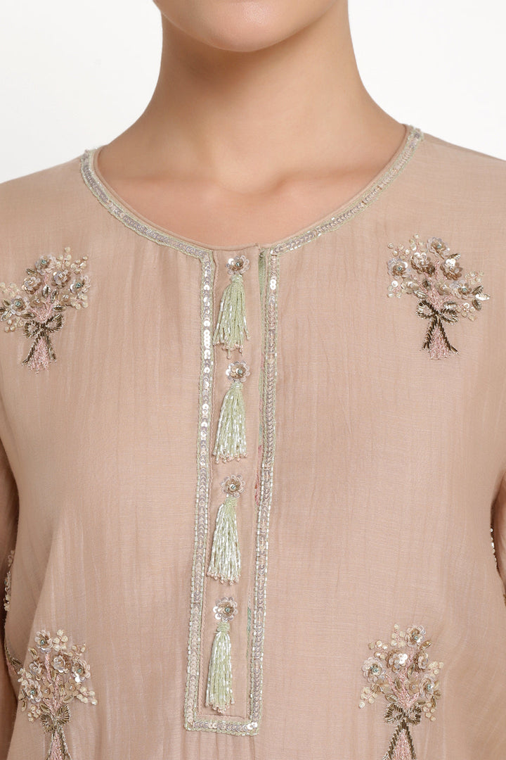 Beige outfit with intricate silver and green embroidery on a plain background