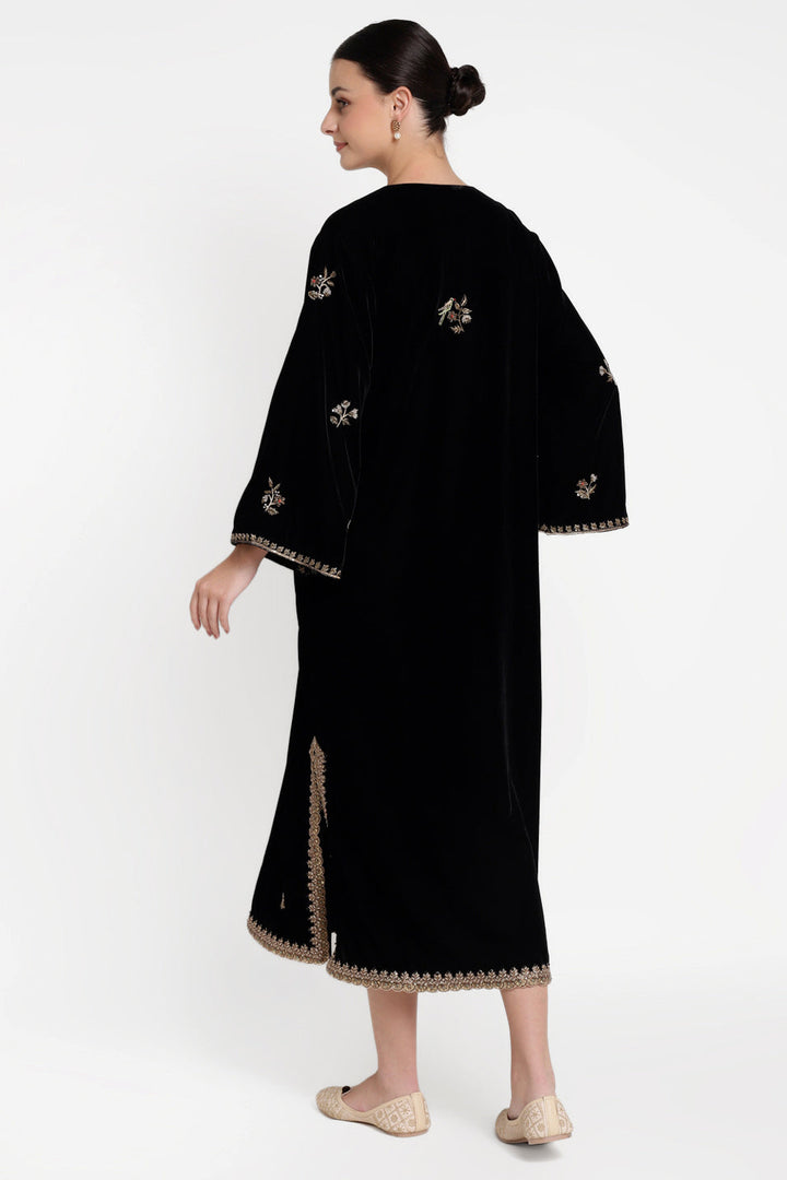 Woman wearing a black dress with gold embroidery on a white background