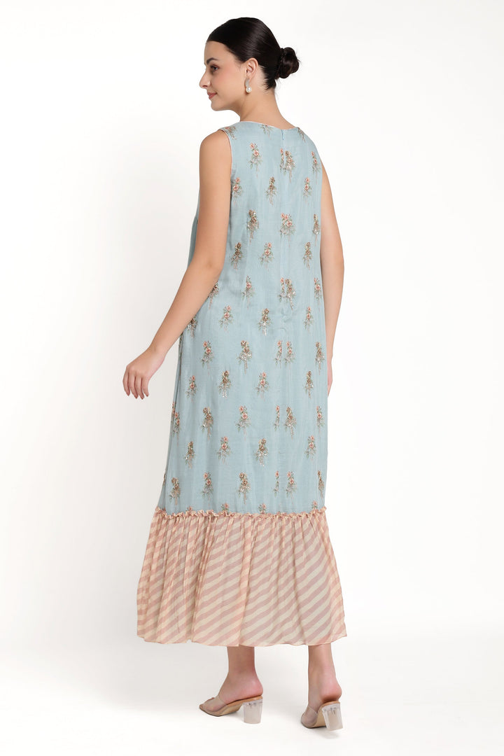 Woman wearing a light blue dress with floral pattern and beige ruffled hem on a white background