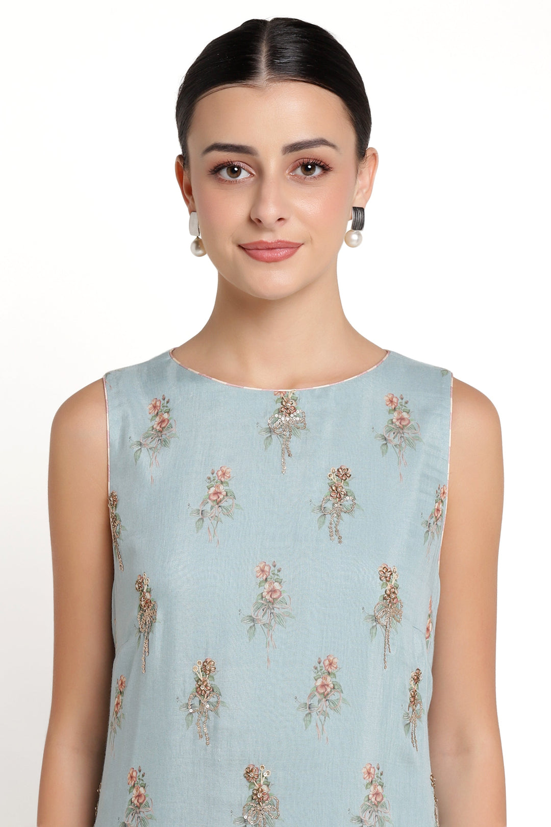 Woman wearing a light blue sleeveless top with floral patterns on a white background