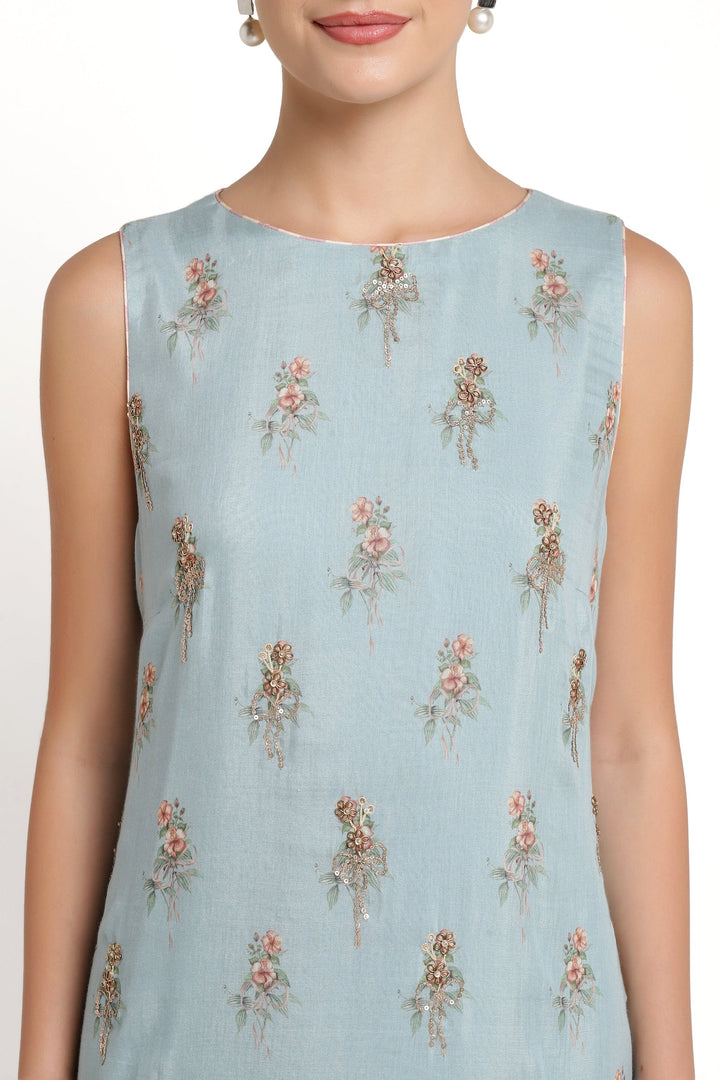 Light blue sleeveless top with floral patterns worn by a model on a white background