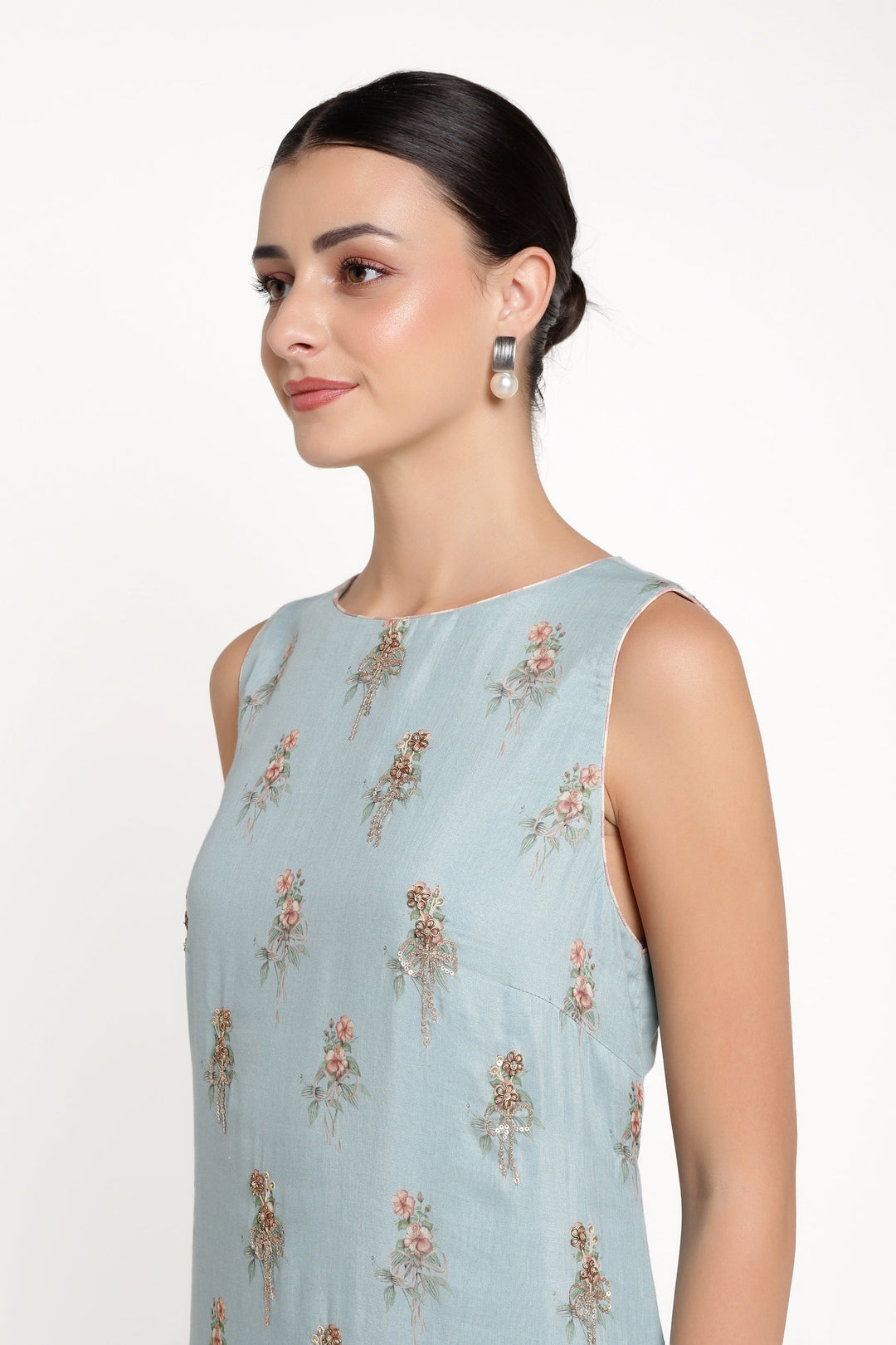 Woman wearing a light blue sleeveless top with floral patterns on a white background
