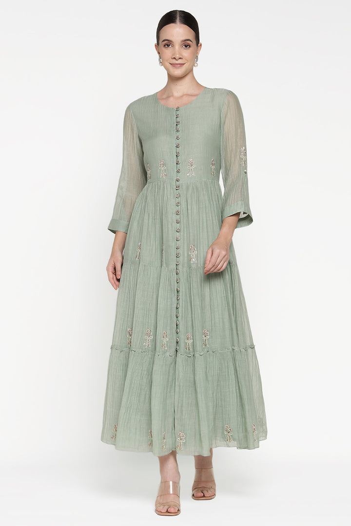 Woman wearing a light green dress with floral embroidery on a white background