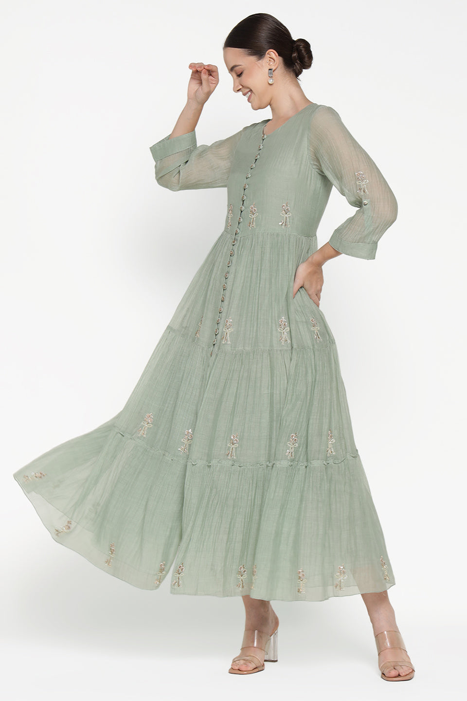 Woman wearing a light green dress with floral embroidery on a white background