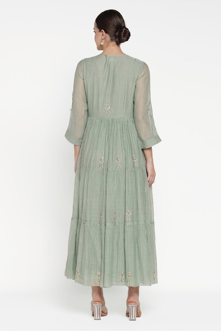 Woman wearing a light green dress with floral embroidery on a white background