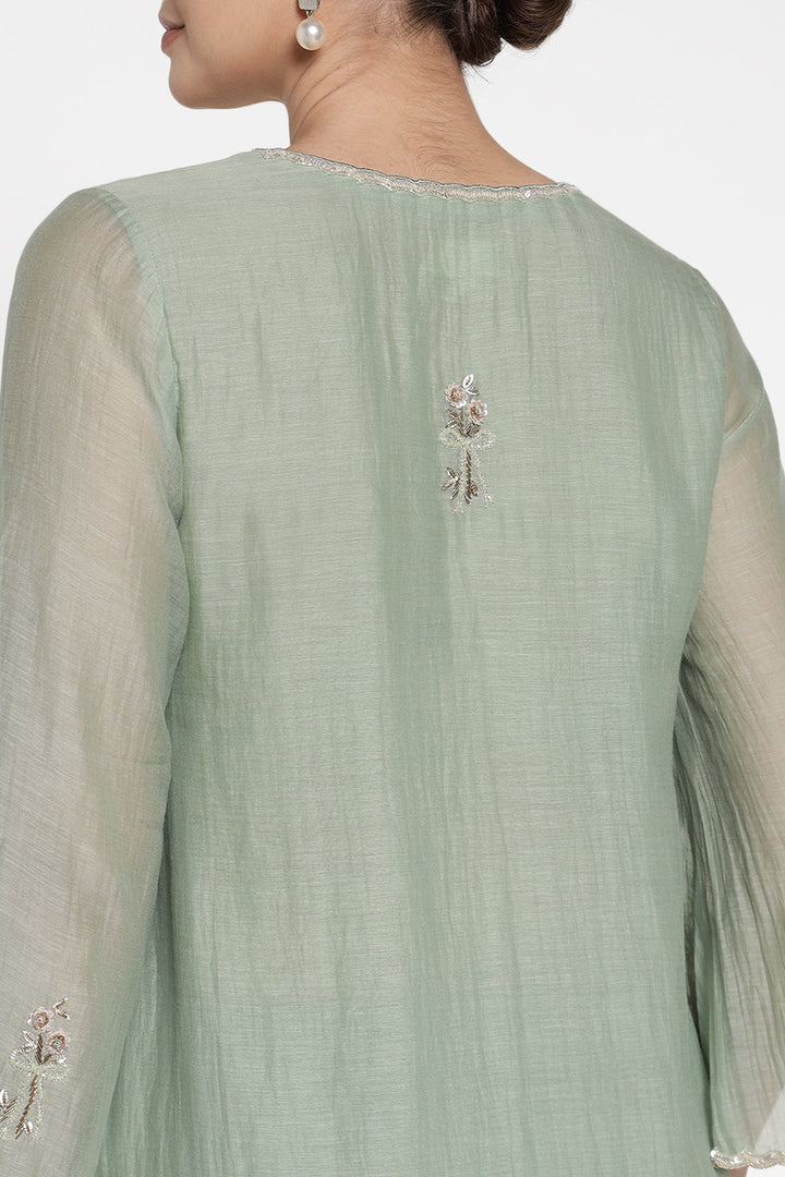 Light green traditional outfit with floral embroidery on a plain background