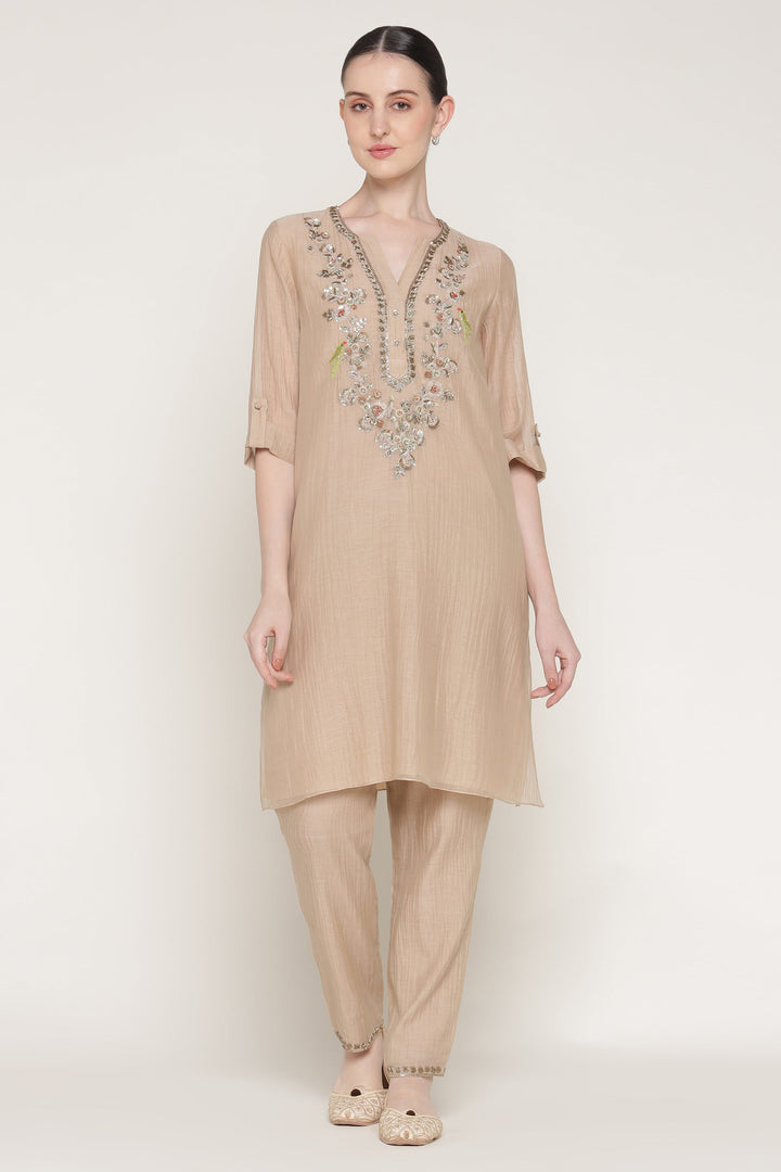 Woman wearing a beige embroidered outfit on a white background