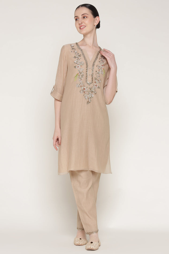 Woman wearing a beige embroidered kurta with pants on a white background