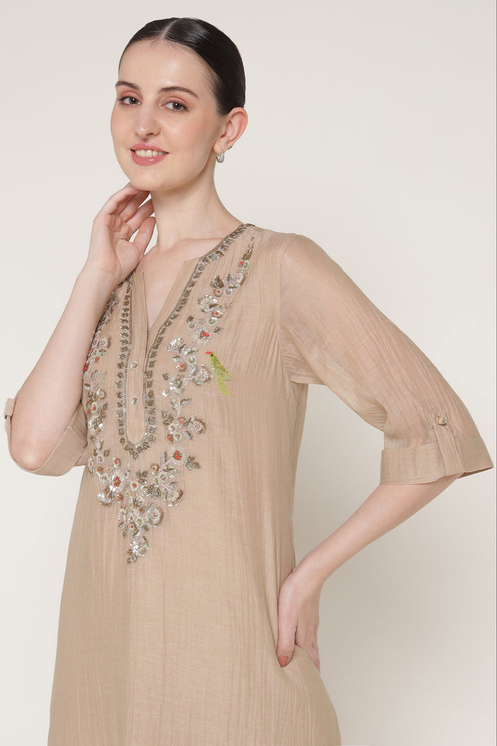 Woman wearing a beige dress with floral embroidery on a plain background