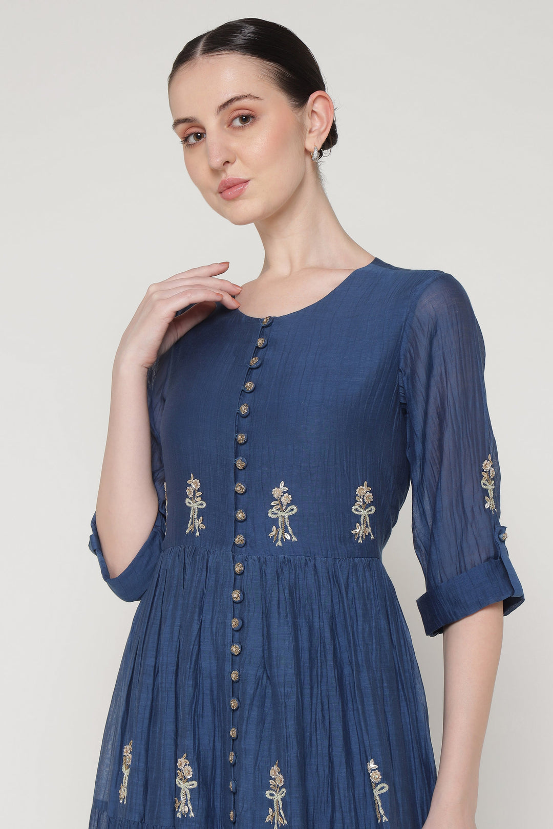 Woman wearing a blue dress with embroidery on a plain background