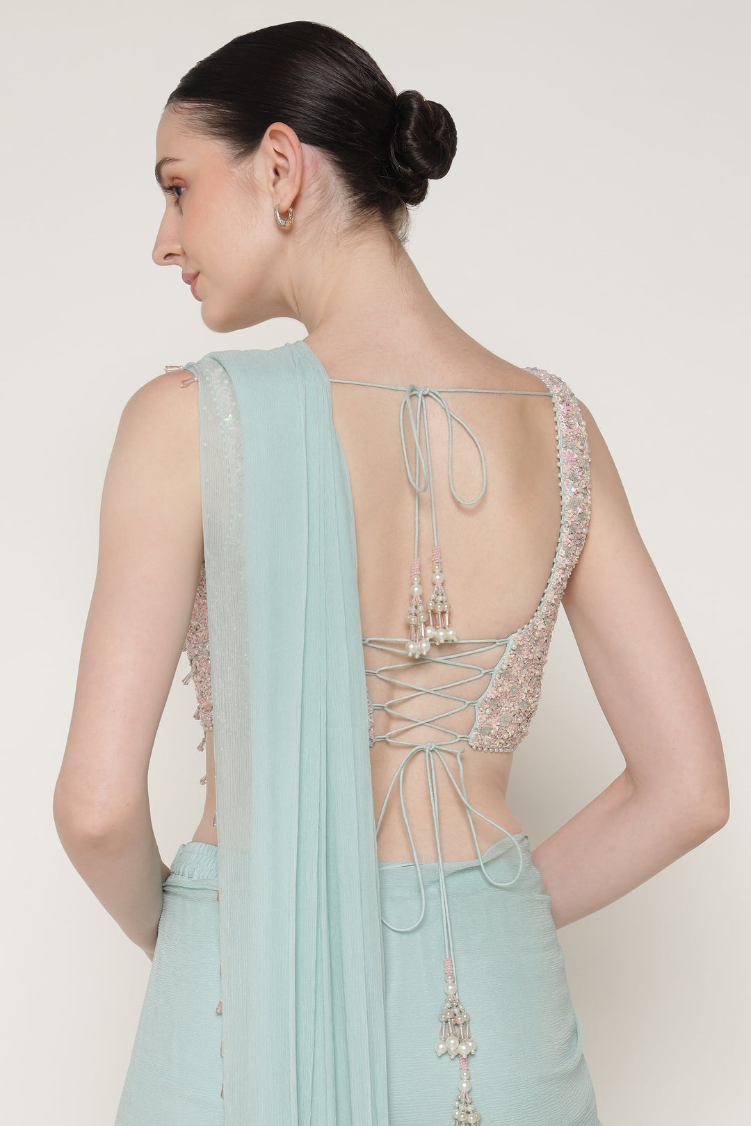 Woman wearing a light blue saree with intricate lace detailing on a plain background