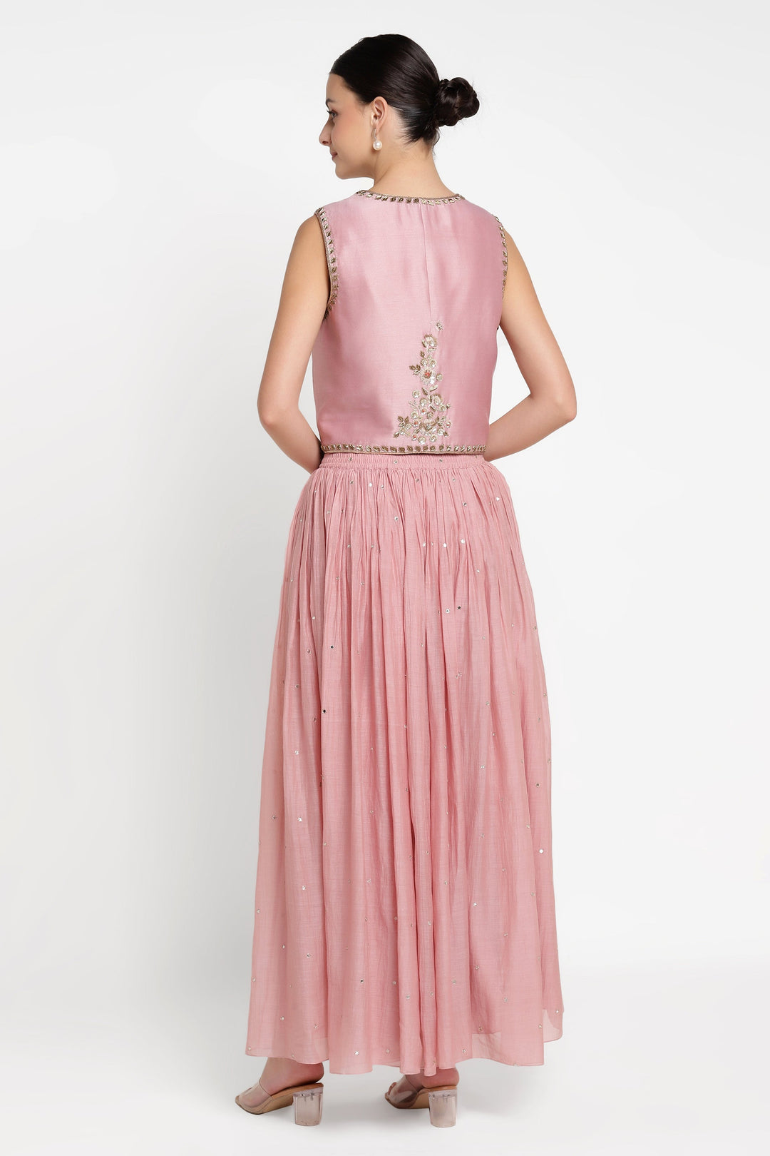 Woman wearing a pink dress with intricate detailing on a white background