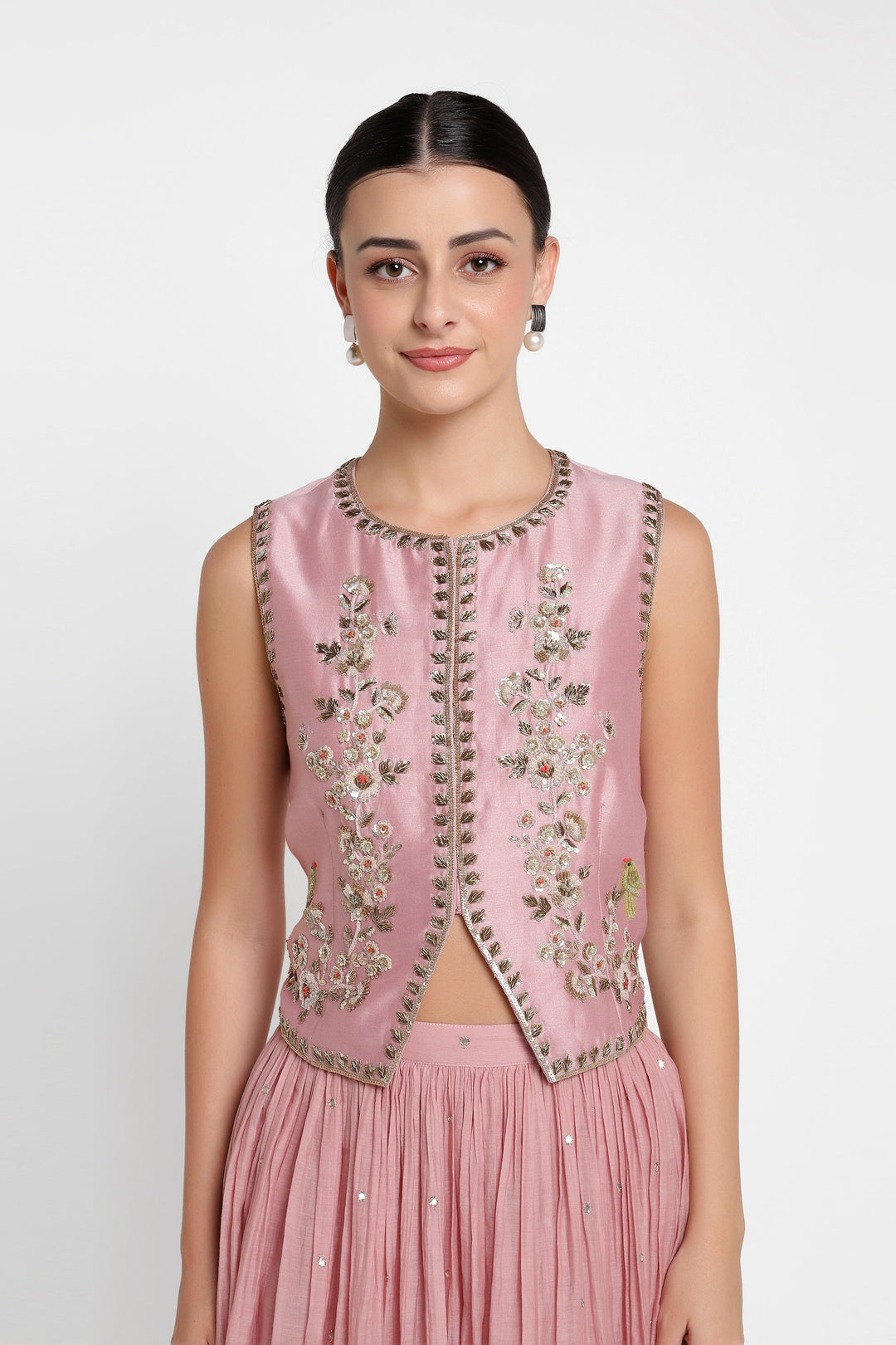 Woman wearing a pink embroidered vest over a matching skirt on a white background