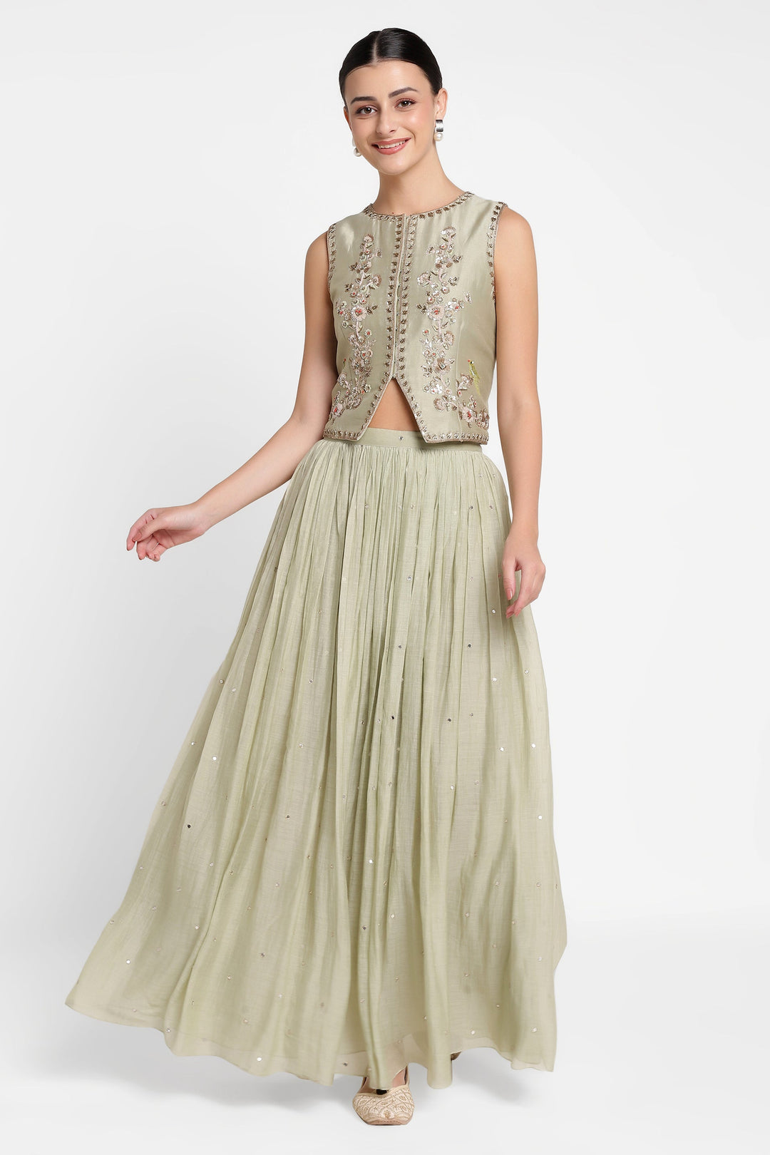 Woman wearing a light green embroidered top and pleated skirt on a white background