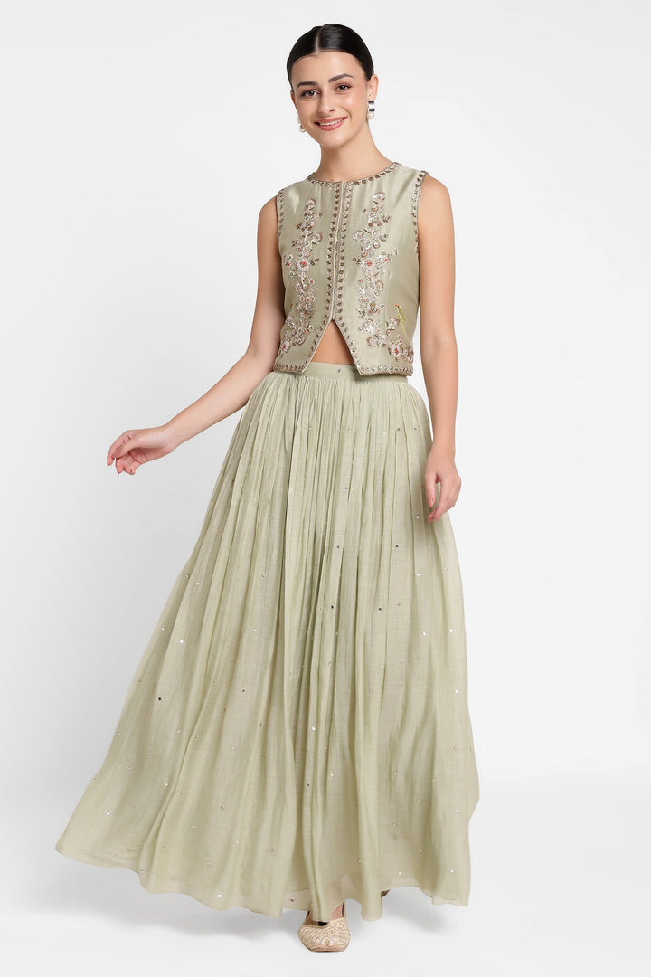 Woman wearing a light green embroidered top and pleated skirt on a white background