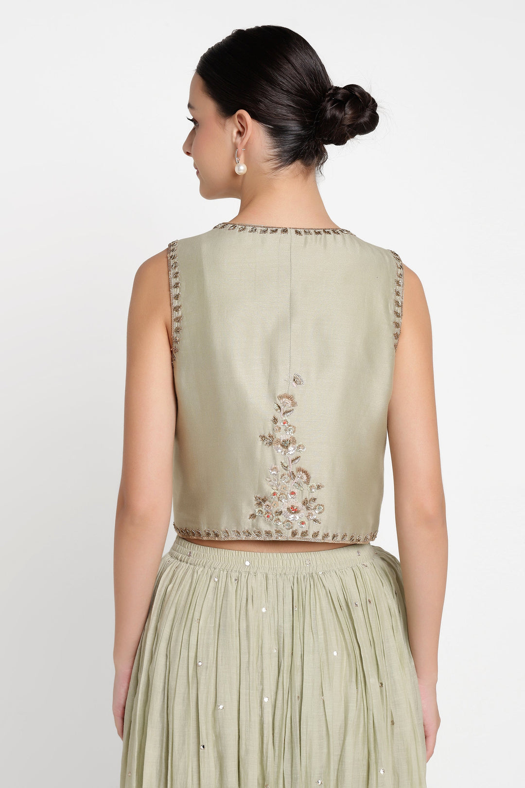 Woman wearing a light green sleeveless top with floral embroidery and a matching skirt on a white background