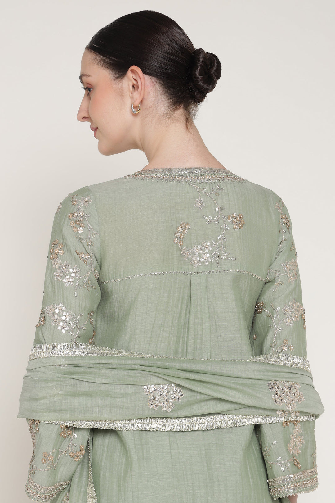 Woman wearing a light green traditional outfit with intricate embroidery on a plain background
