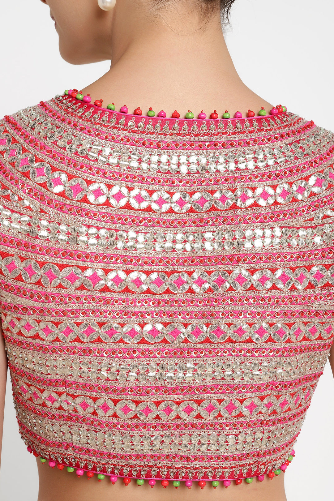 Close-up of a pink and silver embroidered blouse with colorful embellishments on a white background