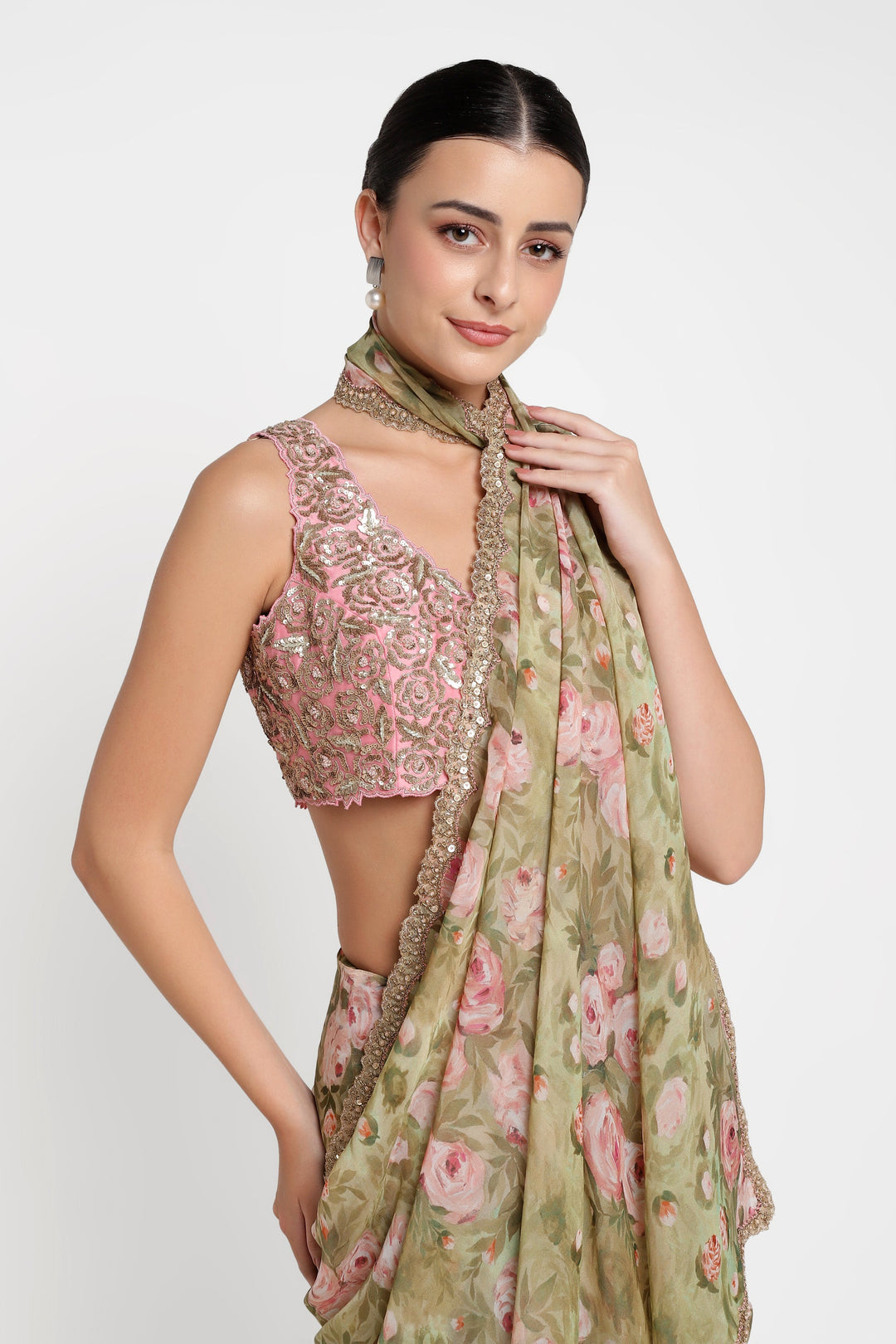 Woman wearing a pink embroidered top and green floral saree against a white background