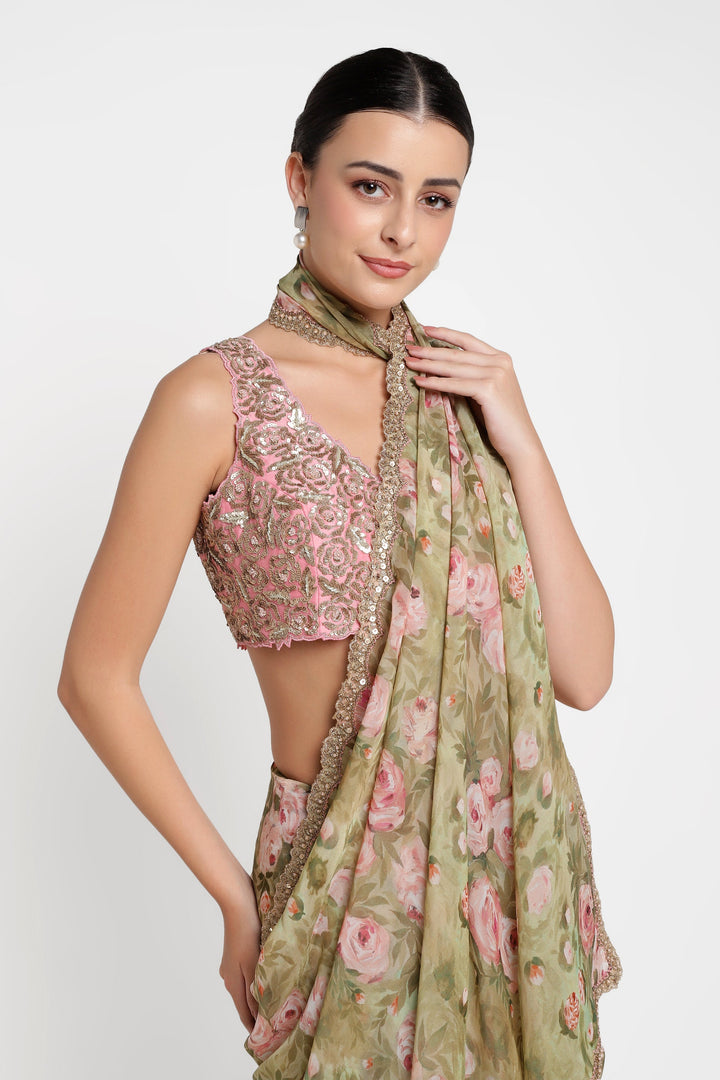 Woman wearing a pink embroidered top and green floral saree against a white background