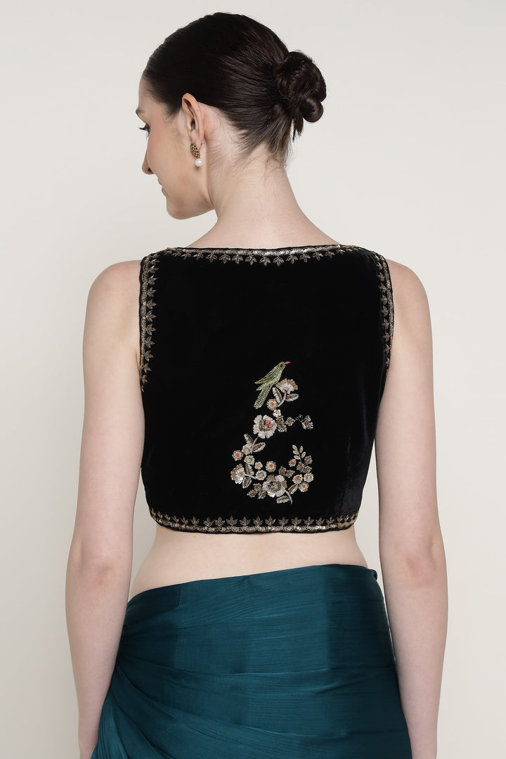 Woman wearing a black embroidered blouse with floral designs on a plain background