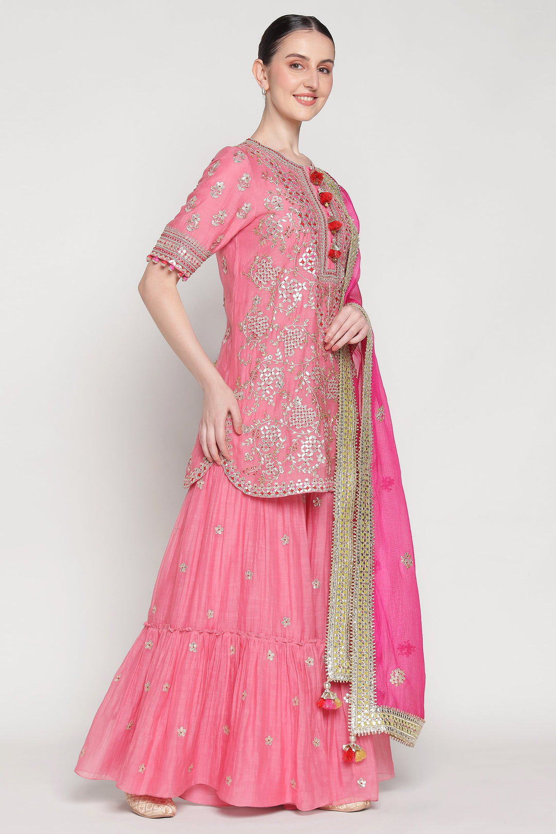 Woman wearing a pink traditional outfit with gold embroidery on a white background