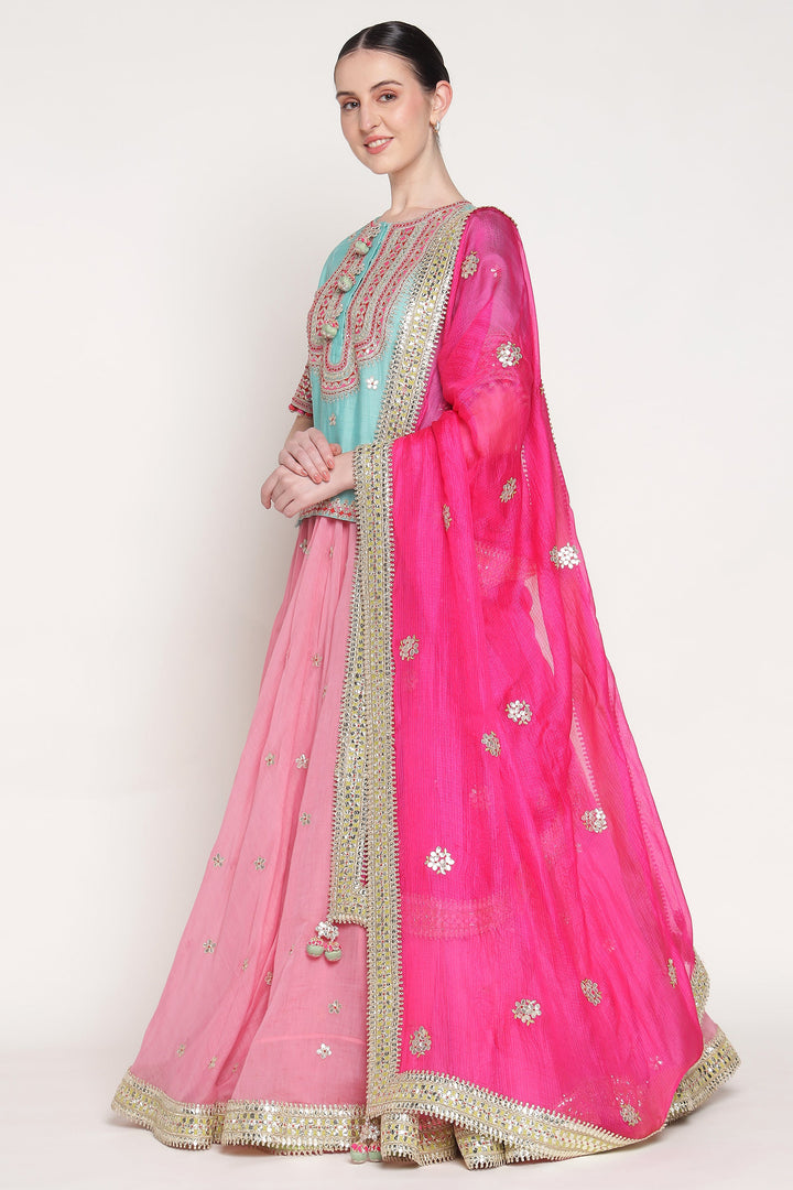 Woman wearing a traditional outfit with a pink dupatta and blue top on a white background