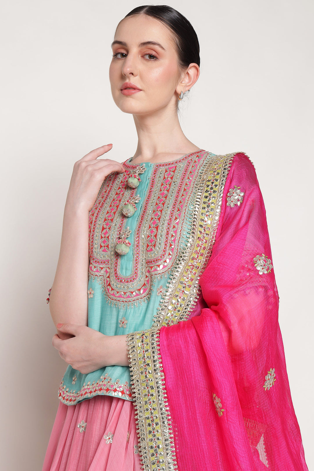 Woman wearing a traditional outfit with pink and turquoise colors on a plain background