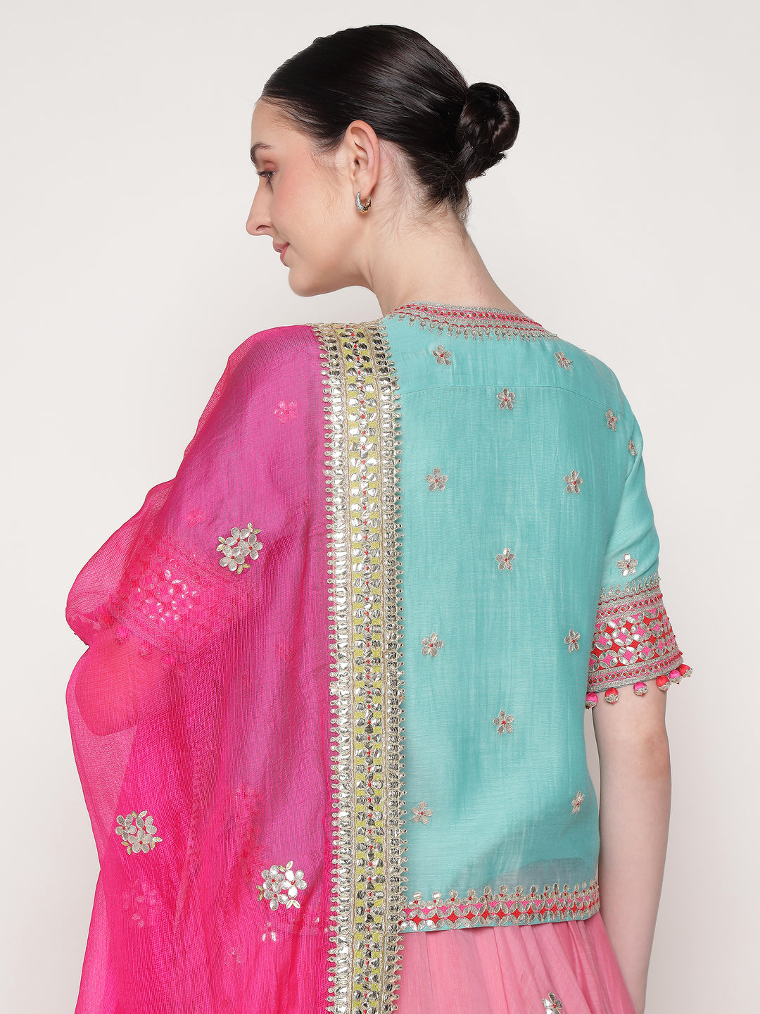 Woman wearing a pink and blue saree with intricate designs on a white background