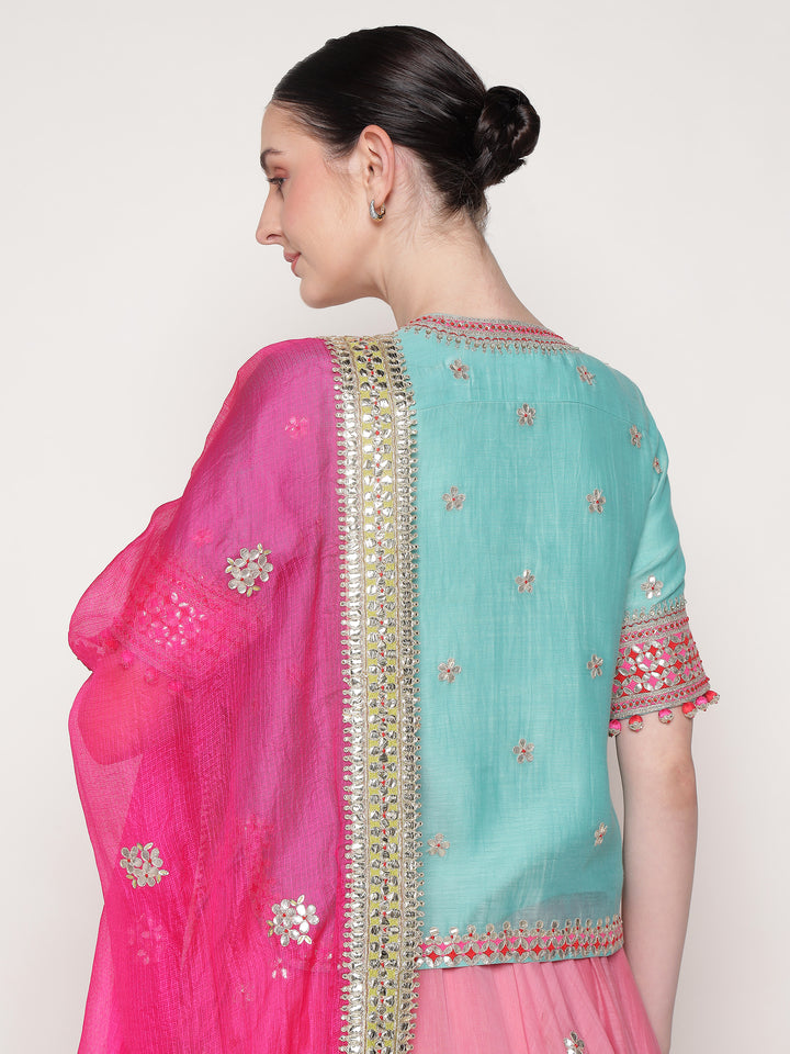 Woman wearing a pink and blue saree with intricate designs on a white background