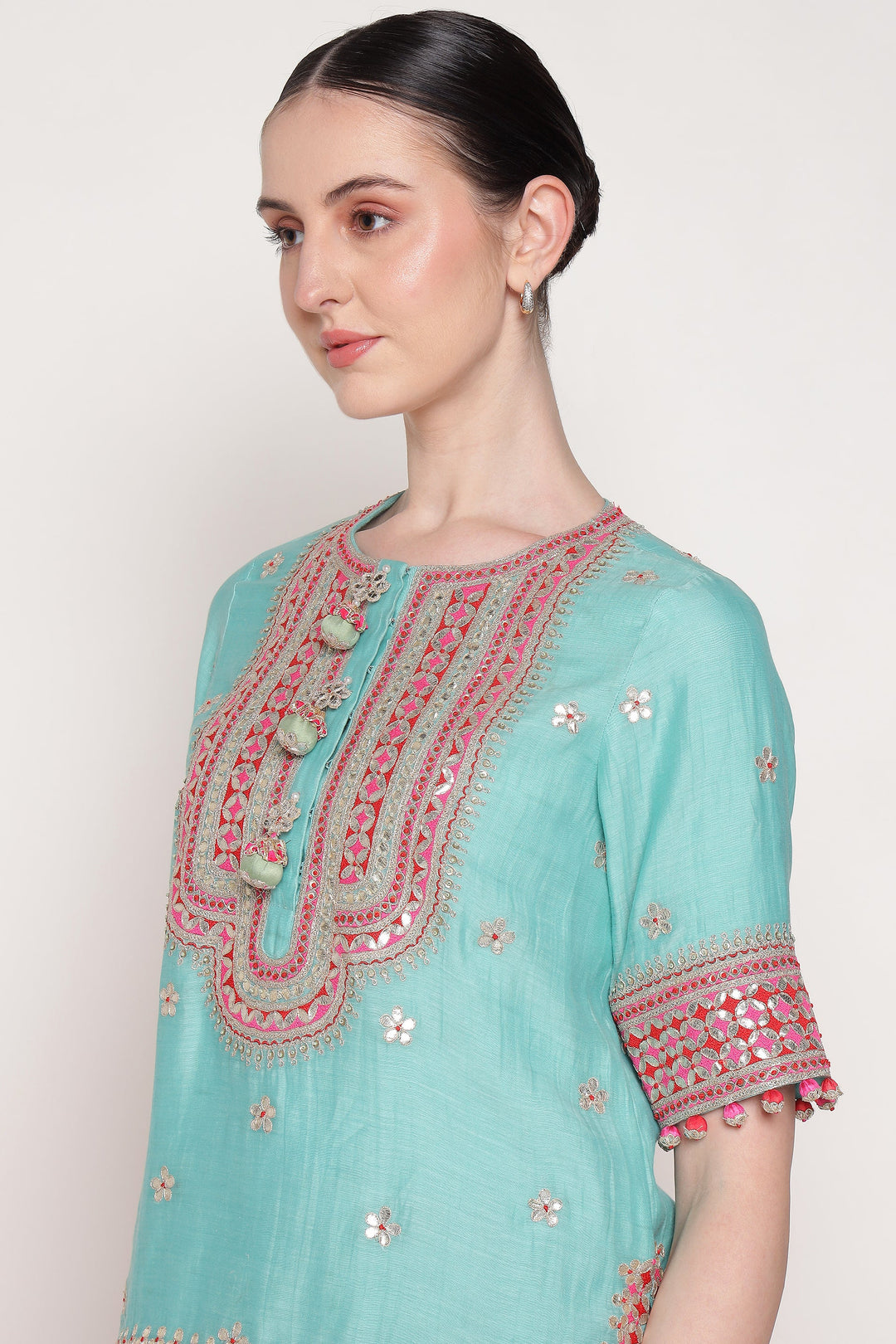 Woman wearing a light blue embroidered dress with pink details on a white background