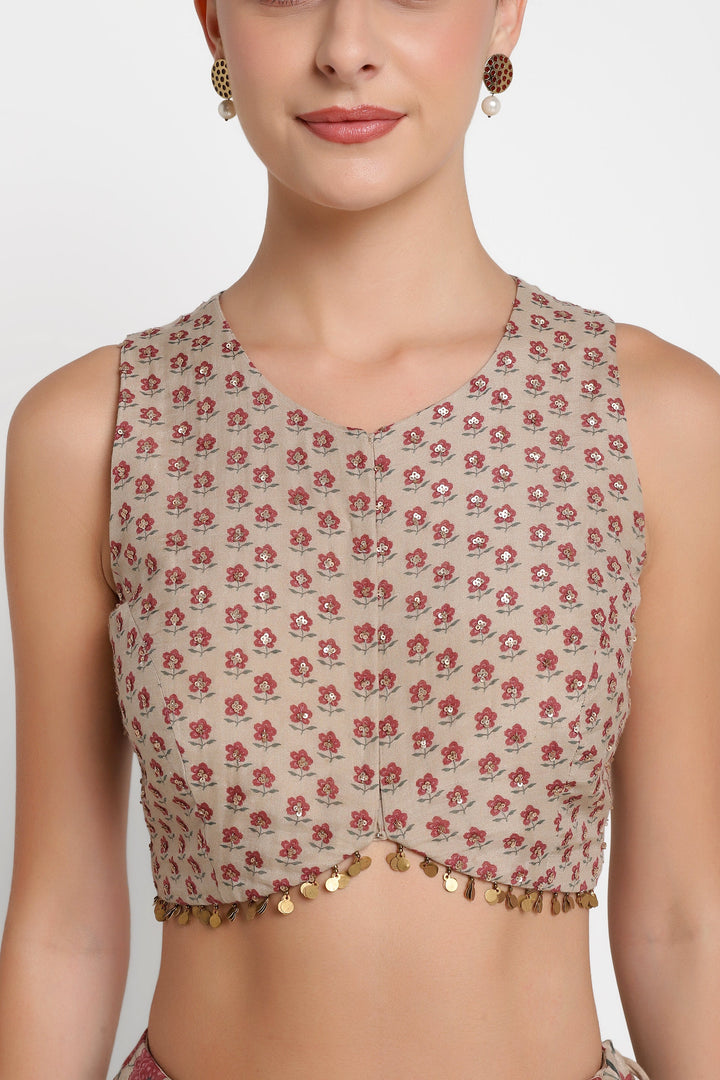 Woman wearing a floral patterned top with gold embellishments on a plain background