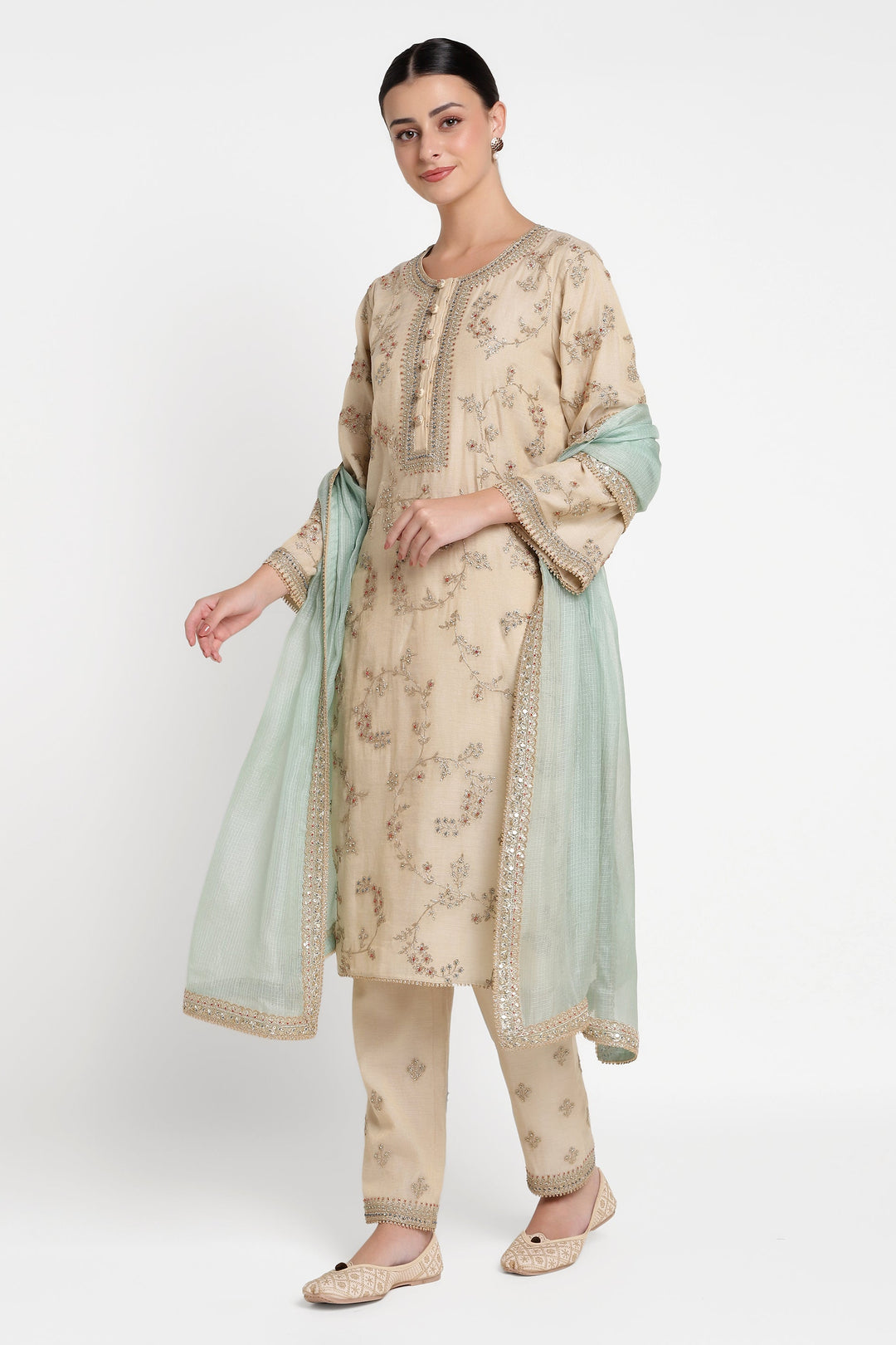 Woman wearing a traditional outfit with a beige kurta, pants, and light green dupatta on a white background