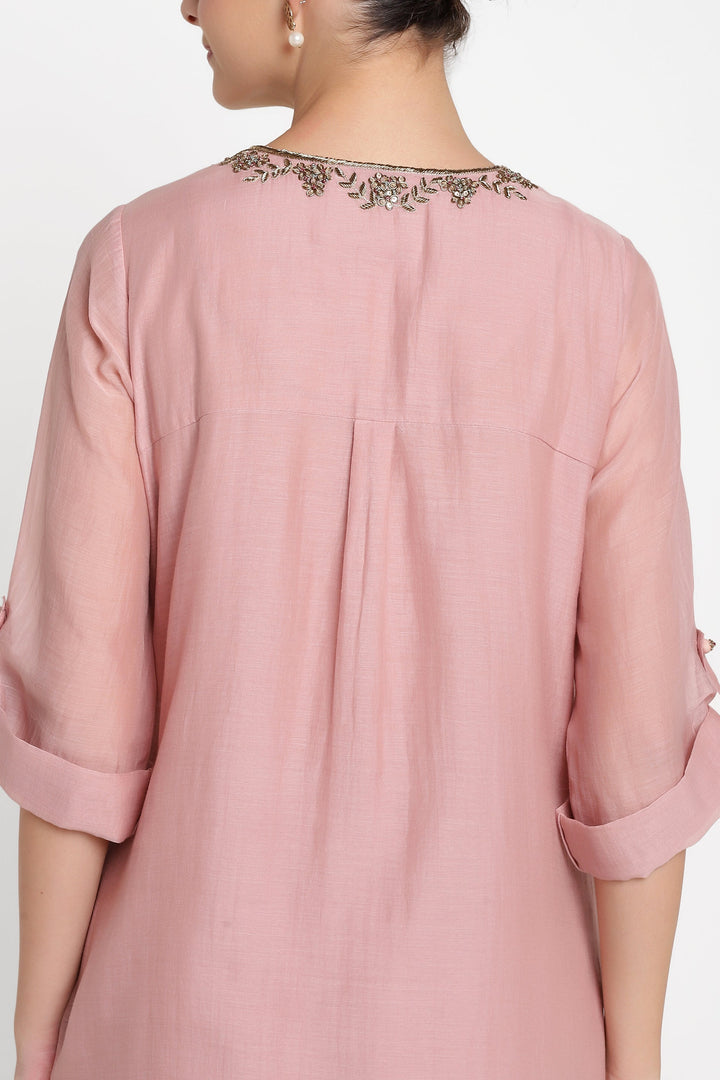 Pink blouse with rolled-up sleeves and intricate detailing on a white background