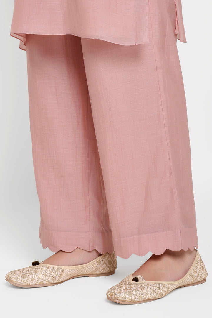 Pink pants with scalloped hem and gold embroidered flats on a white background