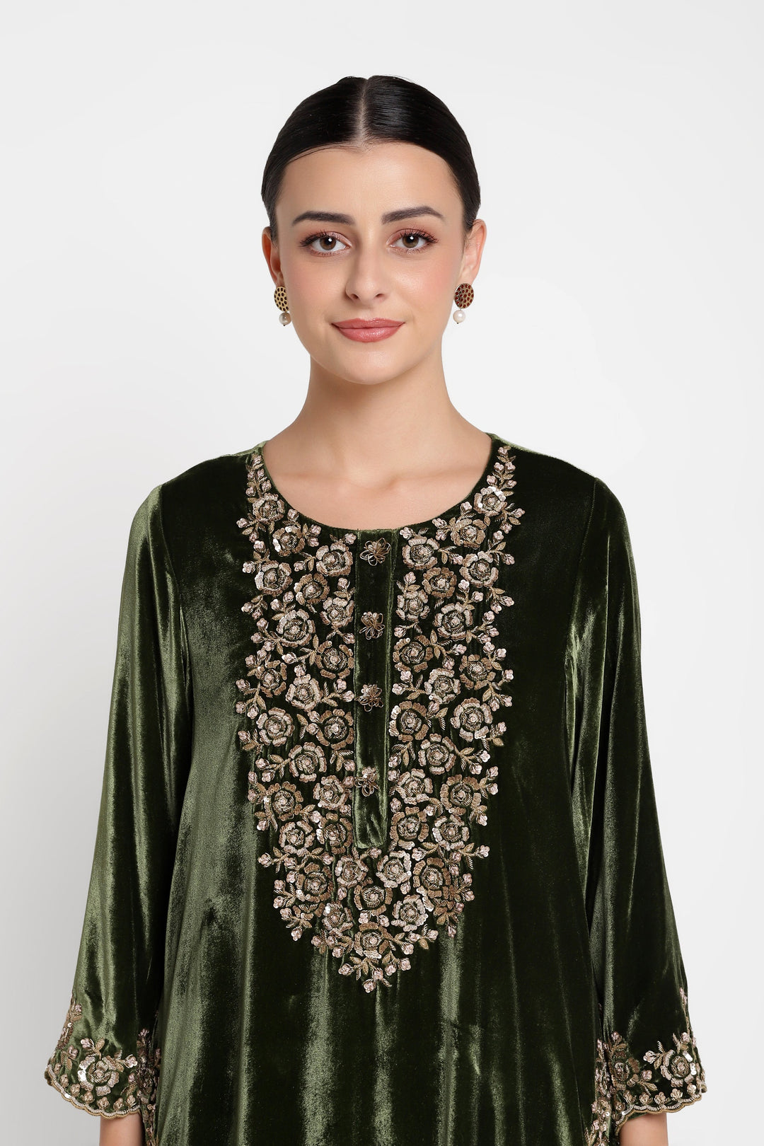 Woman wearing a green velvet dress with intricate gold embroidery on a white background