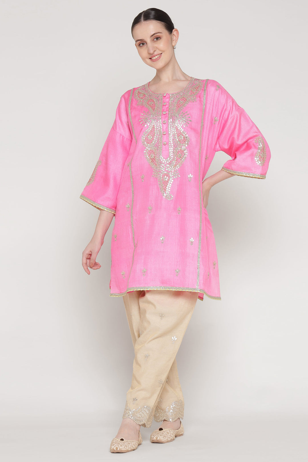 Woman wearing a pink embroidered kurta with beige pants on a white background